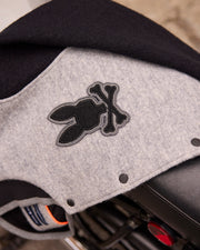 A close-up of a grey fabric featuring a black stitched design of a bunny head crossed with bones. The fabric, likely from the Psycho Bunny MENS TOM WOOL BOMBER JACKET - B6J744D200, appears to drape partially over a black object.