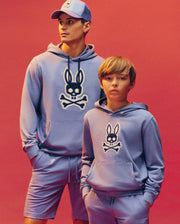 A man and boy pose for a photo in comfy loungewear. The boy wears the Psycho Bunny KIDS RYDER EMBROIDERED BUNNY PATCH HOODIE (KT0500018), adding a playful touch to their relaxed look.