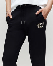 A person wearing Psycho Bunny KIDS WADE CORD PATCH SWEATPANT (KB0800002) with hands in pockets; crafted from a premium cotton blend and featuring "PSY BNY" plus a small graphic printed on the left thigh.