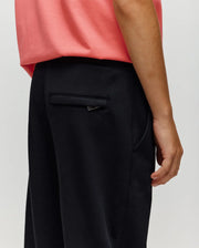 A side view shows a person wearing Psycho Bunny's KIDS WADE CORD PATCH SWEATPANT (KB0800002) in black with a coral pink shirt, highlighting the right arm and back pocket against a plain light background.