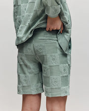 Teen | A child models Psycho Bunny's KIDS KELVIN TOWEL TERRY SWEATSHORT (KB0900002) in textured sage green cotton blend, paired with a matching checkered bunny jacket. The back view shows one hand resting on their hip.