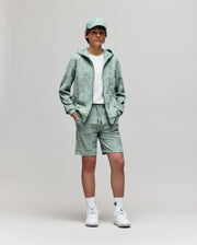 Teen | A young person stands against a plain background, wearing Psycho Bunny's KIDS KELVIN TOWEL TERRY SWEATSHORT (KB0900002) with a white tee, mint green cap and hoodie, and white sneakers, hands in pockets, looking at the camera.
