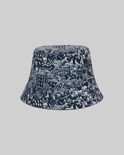 The Psycho Bunny KIDS NAXOS REVERSIBLE BUCKET HAT - KO1500001 features a navy side with white hand-drawn cityscape, buildings, rooftops, skulls, bunnies, and embroidered vents; reverse is a plain gray.