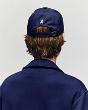 A child with brown hair is seen from behind wearing the Psycho Bunny KIDS MATTEO BASEBALL CAP (KO1500002) in navy cotton twill, featuring a small white bunny logo above the adjustable strap.