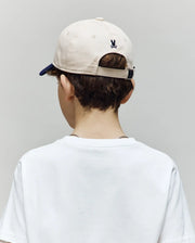 A child with short brown hair, in a white t-shirt and the Psycho Bunny KIDS MATTEO BASEBALL CAP (KO1500002) in beige with a small black logo, is shown from behind against a plain light gray background.