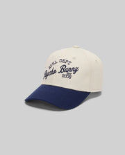 The KIDS MATTEO BASEBALL CAP (KO1500002) by Psycho Bunny features white cotton twill, a navy brim, varsity-style "ATHL DEPT Psycho Bunny EST. 2005" embroidery in navy, an adjustable strap, and is shown on a plain gray background.