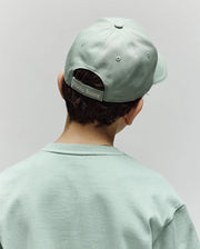 A child is seen from behind wearing a light green Psycho Bunny KIDS DEREK BASEBALL CAP (KO1500008) and a matching premium cotton sweatshirt. The cap features a "Psycho Bunny" label on its adjustable strap, set against a plain, light-colored background.