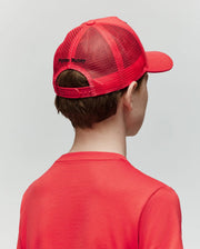 A child is seen from behind wearing the Psycho Bunny KIDS GLENN TRUCKER CAP - KO1500012 in bright red, featuring an adjustable snapback and black embroidery, paired with a matching red shirt against a plain light background.