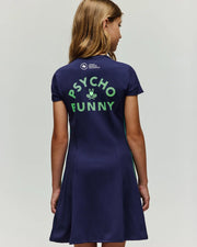 A young girl with light brown hair faces away, wearing the Psycho Bunny RETAIL BALL CREW GIRLS DRESS (FR) in navy. The back features green "PSYCHO FUNNY" lettering and a small graphic of a tennis ball with two rackets.