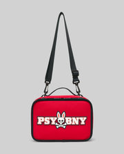 The PSYCHO BUNNY LUNCH BOX - KO2400002 by Psycho Bunny is a rectangular red insulated lunch box with an adjustable black strap, white bunny skull and crossbones logo, and "PSYBNY" text on the front. Background is light gray.