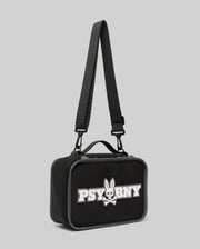 The PSYCHO BUNNY LUNCH BOX - KO2400002 by Psycho Bunny is a black rectangular bag with a handle and adjustable shoulder strap, featuring a white "PSYBNY" logo and a silicone Bunny skull and crossbones on the front. Background: light gray.