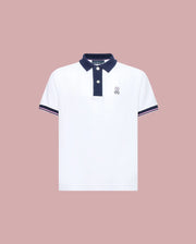 The Psycho Bunny KIDS ARCHIVE CLASSIC BUNNY PIQUE POLO (KT0100010) is a white, short-sleeve Pima cotton shirt with a navy collar and trim, three dark buttons, and an embroidered Bunny logo on the left chest, shown on a pale pink background.