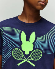 A child wears the Psycho Bunny RETAIL BALL CREW YOUTH TEE (FR) - KT0200042, a navy blue shirt featuring a neon green bunny head and crossed tennis rackets graphic with curved blue and green lines.