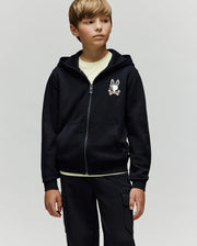 A young boy with light brown hair wears the Psycho Bunny KIDS WADE CORD PATCH ZIP HOODIE (KT0500016) in black, featuring an embroidered hood and bunny logo, paired with matching black cargo pants and a light shirt against a plain background.