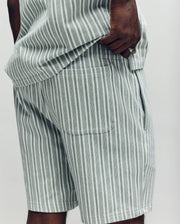 A person wears Psycho Bunny's MENS ROBERT KNIT STRIPE SHORT (MB0900007) in light gray and white stripes, paired with a matching knit cotton top. The photo, cropped to the torso and upper legs, shows one hand tucked in a pocket.
