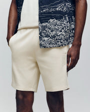 Wearing Psycho Bunny's MENS LAZSLO SWEATSHORT - MB0900016 with a white tee and dark patterned short-sleeve shirt, a person stands hands-in-pocket against a plain background, exemplifying effortless casual style.