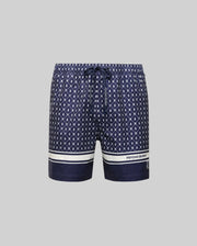 The MENS HUNTER ALL OVER PRINT SWIM TRUNK - MB1000011 from Psycho Bunny features navy blue quick-dry fabric, a white geometric bunny print, drawstring waist, white hem stripes, and branding on the lower left leg, shown on a light gray background.