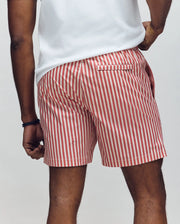 A person is seen from behind, waist down, wearing Psycho Bunny MENS ZANE SWIM TRUNK - MB1000030 featuring red and white vertical stripes and a no-chafe net for comfort, paired with a white T-shirt, resting one hand on their hip.