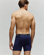A shirtless man is shown from the back wearing navy blue Psycho Bunny MENS 3 PACK BOXER BRIEF - MO1400006, featuring a black waistband with "PSYCHO BUNNY" text and bunny logos in white. The plain light background highlights all-day comfort.