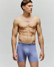 A fit, shirtless man with short brown hair models Psycho Bunny’s MENS 3 PACK BOXER BRIEF - MO1400006 in light purple cotton-modal with a blue logo waistband and bunny logos, offering all-day comfort, against a plain light background.