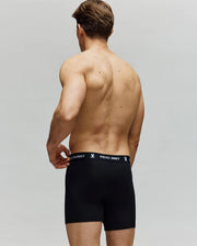 A shirtless man, seen from behind, wears Psycho Bunny MENS 3 PACK BOXER BRIEF (MO1400006) in black with a logo and bunny symbol waistband, made from premium cotton-modal, against a plain light gray background.