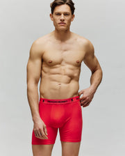 A muscular man wearing Psycho Bunny’s MENS 3 PACK BOXER BRIEF - MO1400006 stands shirtless against a plain background, looking forward with a neutral expression and one hand resting near his waist.