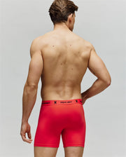 A man faces away, displaying his bare back and wearing bright red Psycho Bunny MENS 3 PACK BOXER BRIEF - MO1400006 with logo waistband, made from premium cotton-modal for all-day comfort against a plain gray background.