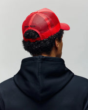 A person is seen from behind against a plain light background, wearing a black hoodie and the Psycho Bunny MENS GLENN TRUCKER CAP - MO1500004, a red mesh trucker cap with an adjustable snapback.