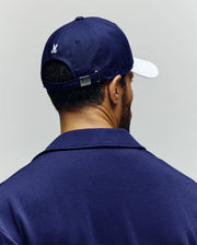 A man is seen from behind wearing a navy blue cotton twill jacket and the Psycho Bunny MENS MATTEO BASEBALL CAP (MO1500008) in navy, featuring a white brim, embroidered wordmark, white bunny logo on the back, and an adjustable metal strap.