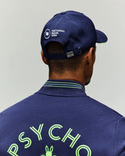 A person is seen from behind wearing a Psycho Bunny TENNIS BALL CREW MENS CAP ENGLISH (MO1500024) with the "National Bank Open" logo and a matching jacket displaying "PSYCHO" in light green. The background is plain and light-colored.