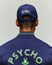 A person, seen from behind, wears a navy Psycho Bunny jacket with "PSYCHO" and a tennis bunny logo, plus the Psycho Bunny TENNIS BALL CREW MENS CAP FRENCH (MO1500025) featuring "OMNIUM BANQUE NATIONALE" on breathable mesh.