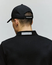 A person is seen from the back against a plain light background, wearing the Psycho Bunny MENS FORREST SPORT CAP (MO1500051) and a black polo shirt, both featuring Psycho Bunny branding.