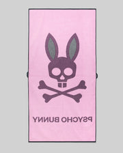The Psycho Bunny MENS CLASSIC BUNNY TOWEL (MO1700004) is pink, showcasing a large dark gray bunny skull and crossbones with "PSYCHO BUNNY" below, all set against a plain gray background.