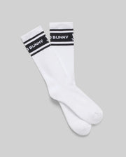 The Psycho Bunny MENS 3 PACK SPORT SOCK - MO2200006 features white Pima cotton crew socks with black bands, white text, and a small bunny logo. Inspired by vintage motifs, they're displayed flat on a light gray background.