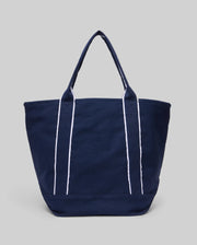 The Psycho Bunny MENS CANVAS TOTE BAG - MO2400016 is a navy tote with two handles and vertical white stripes, built for function, shown on a light gray background.