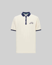 The Psycho Bunny MENS MATTEO PIQUE POLO (MT0100024) is a cream Pima cotton short-sleeve shirt with a navy collar, cuffs, and button placket featuring Mother-of-Pearl buttons. Navy cursive text accents the left chest; shown on a gray background.