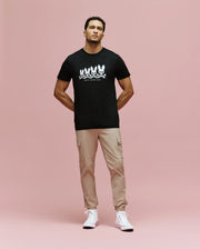 A man stands against a pink background wearing the Psycho Bunny MENS ARCHIVE GRADIANT BUNNY GRAPHIC TEE (MT0200029), paired with beige cargo pants and white high-top sneakers. He faces forward with his hands in his pockets.