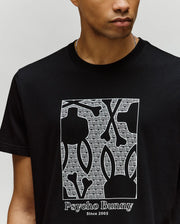 A person wears the Psycho Bunny MENS GLENN GRAPHIC TEE (MT0200034), a black Pima cotton tee with a white outlined bunny and repeated "PB" letters, plus "Psycho Bunny Since 2005" printed below the graphic.