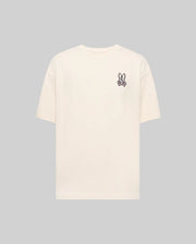The Psycho Bunny MENS WADE OVERSIZED FIT CHEST TEE - MT0200152 is a plain beige Pima cotton tee with a small cartoon bunny face patch on the left chest, shown against a light gray background.