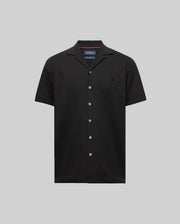 The Psycho Bunny MENS JAYME KNIT SEERSUCKER CABANA COLLAR SHIRT (MT0300002) is a black short-sleeve cotton-blend shirt with a cabana collar, white buttons, and an embroidered logo on the left chest, shown on a light gray background.