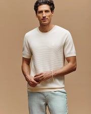 A man with short dark hair wears the Psycho Bunny MENS MARIO STRIPED SWEATER T-SHIRT (MT0400009) and light gray pants, standing against a beige background facing the camera with a relaxed expression.