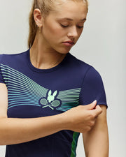 A woman in the Psycho Bunny TENNIS BALL CREW WOMENS DRESS ENGLISH - WO2000004, a navy moisture-wicking shirt with green and blue stripes and a bunny logo with tennis rackets, looks down while adjusting her short sleeve.