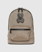 The Psycho Bunny DOME BACKPACK - B6A628Z1BP is a beige dome backpack with a black zipper, bold black Psycho Bunny logo above crossed bones, front zip pocket, top handle, and padded laptop compartment for convenience.