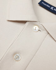 The Psycho Bunny MENS CLASSIC PIQUE POLO SHIRT - B6K001B200 in beige is crafted from luxurious Pima cotton with textured fabric. It features a collar, two white buttons, and a visible blue text label inside, embodying timeless men's fashion elegance.