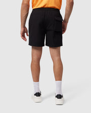 A person wearing a bright orange shirt, Psycho Bunny's MENS MALTA HYDROCHROMIC SWIM TRUNK - B6W321B2SW featuring a pocket on the right side, white crew socks, and white sneakers is standing against a plain white background. The image is taken from the back, showcasing the apparel.
