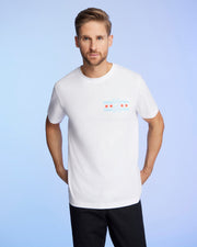A person with light brown hair and a beard is wearing the Psycho Bunny MENS CHICAGO CITY TEE - B6U551W1PC in soft Pima cotton. The shirt has a graphic design of red stars and blue stripes on the chest against a light blue gradient background.