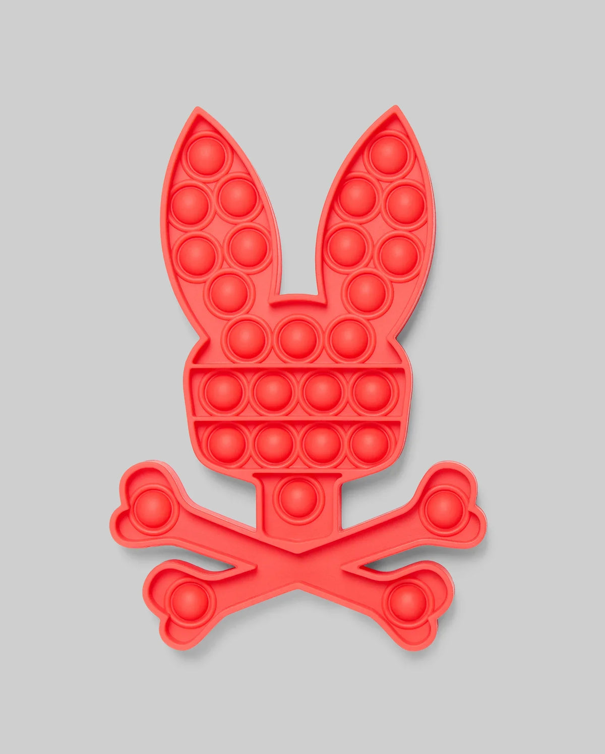 The Psycho Bunny PSYCHO BUNNY POP IT - B0A376E200 is a red silicone pop-it toy shaped like a bunny's head above crossed bones, blending stress relief with playful, skull-and-crossbones-inspired design.