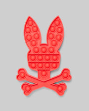 The Psycho Bunny PSYCHO BUNNY POP IT - B0A376E200 is a red silicone pop-it toy shaped like a bunny's head above crossed bones, blending stress relief with playful, skull-and-crossbones-inspired design.