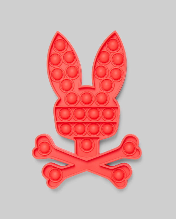 The Psycho Bunny PSYCHO BUNNY POP IT - B0A376E200 is a red silicone pop-it toy shaped like a bunny's head above crossed bones, blending stress relief with playful, skull-and-crossbones-inspired design.