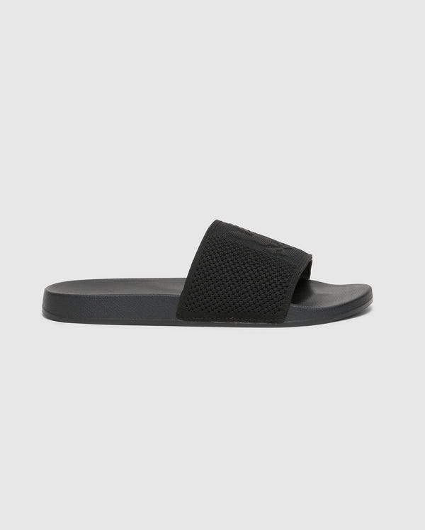The Psycho Bunny KIDS KNIT SLIDES - B0A377F200 is shown in profile against a white background. This black slide sandal has a textured strap, flat sole, and molded footbed for comfort, all in a minimalist design ideal for poolside lounging.